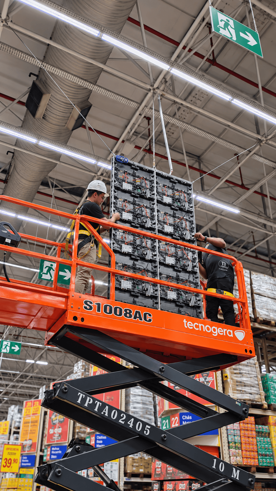 Dois técnicos da Tiagora em plataforma elevatória montando um painel de LED em altura dentro de uma loja
